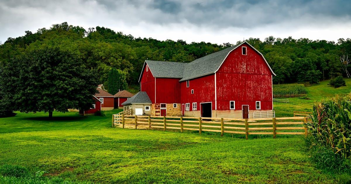 Red farm barn on green pasture, illustrating Kioti vs Yanmar vs LS compact tractor brand comparison for value buyers