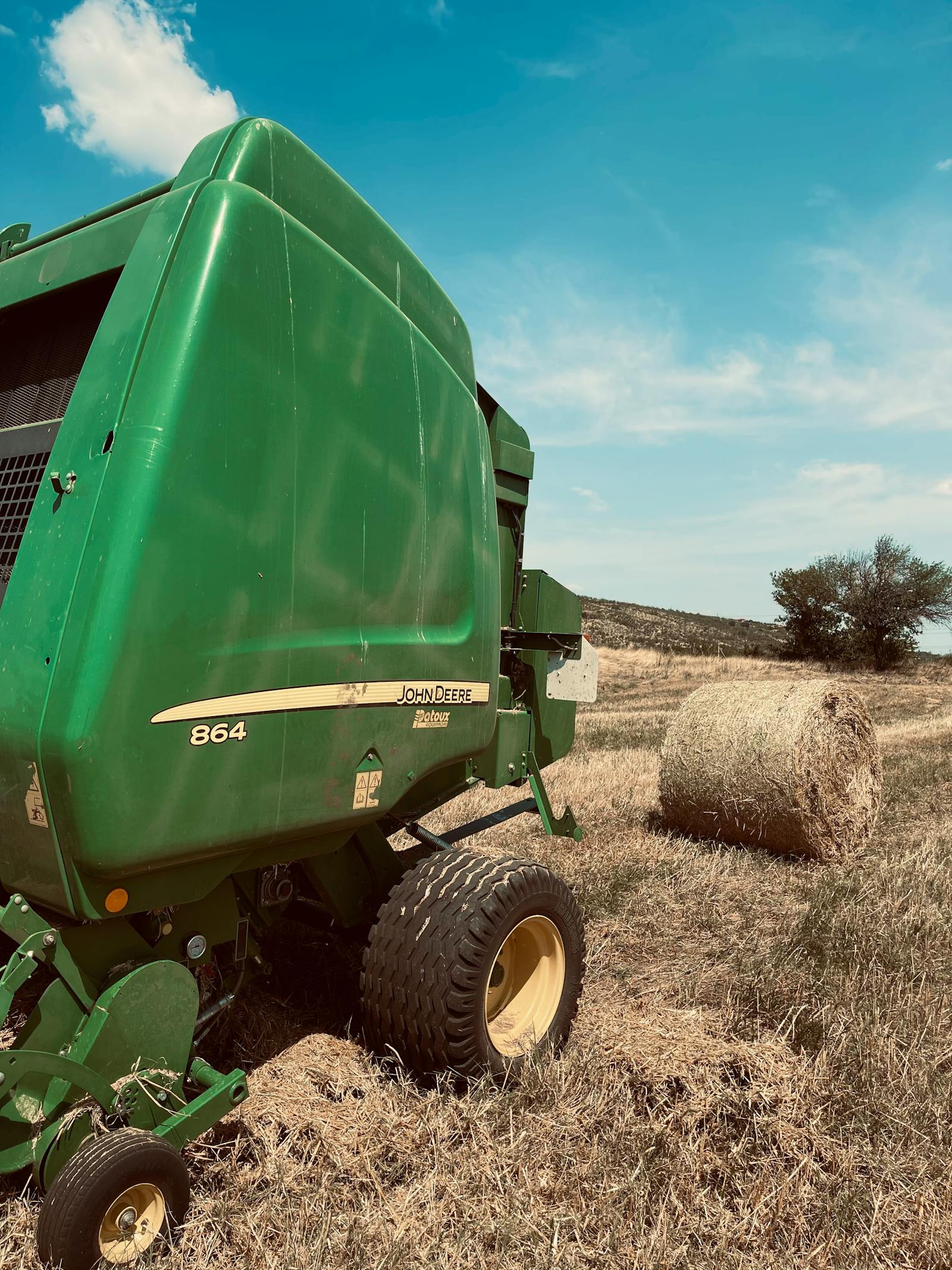 Used round baler in a hay field with a finished round bale on the ground